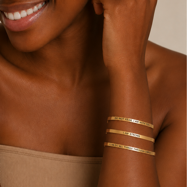 A close-up lifestyle shot of a smiling woman wearing three slim gold bangles on her wrist. The bangles feature engraved text including 'LOVE', 'BELIEVE', and 'PERSIST'.